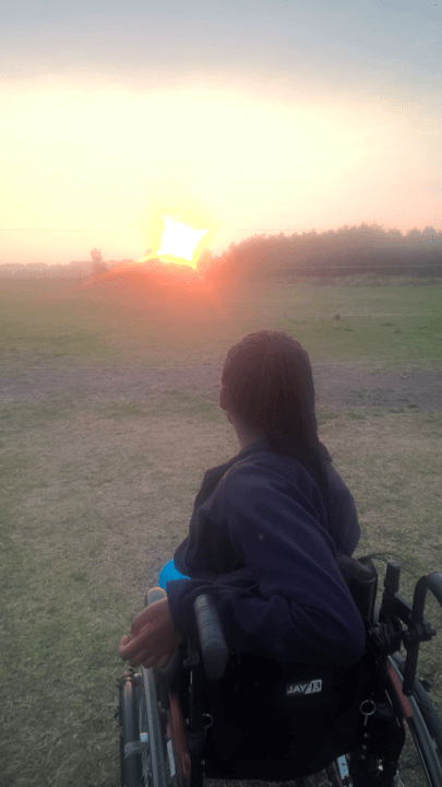 A picture of me from behind with the sunset in front of me and my wheelchair in a wide, open field